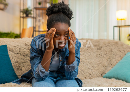 African American woman massaging head on sofa with frustration from headache after studying hard 139262677