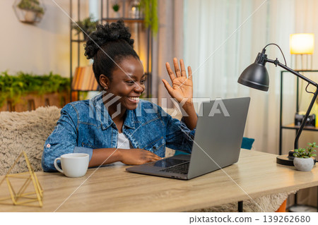 African American woman waving hand while chatting with friends conversation online on laptop at home African American woman waving hand while chatting with friends conversation online on laptop at home 139262680