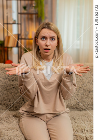 Adult woman spreading hands at home on sofa, showing frustration and dissatisfaction after bad news 139262732