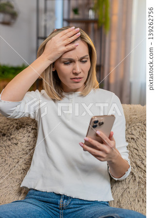Adult woman disappointed by bad news on smartphone at home sighs with frustration emotional reaction 139262756
