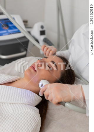 Woman receives RF lifting facial massage therapy from cosmetologist using professional equipment Woman receives RF lifting facial massage therapy from cosmetologist using professional equipment 139262919
