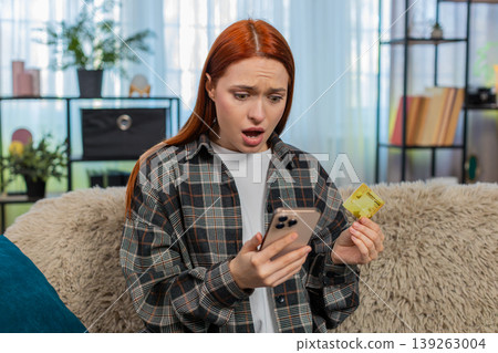 Woman sitting on sofa checking credit card balance on phone looking anxious about blocked account 139263004