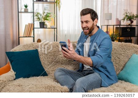 Man laughing while reading funny social media comments on smartphone, relaxing on comfortable sofa 139263057