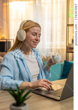 Young woman working from home on sofa, wireless headphones, tea sip, laptop focus, relaxed vibe Young woman working from home on sofa, wireless headphones, tea sip, laptop focus, relaxed vibe 139263067