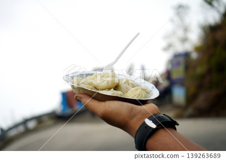Hand holding a plate of steamed momos dumplings with a blurred mountain background 139263689