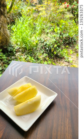 Three fresh sliced apples arranged on a white plate against a lush, natural background. Three fresh sliced apples arranged on a white plate against a lush, natural background. 139263875