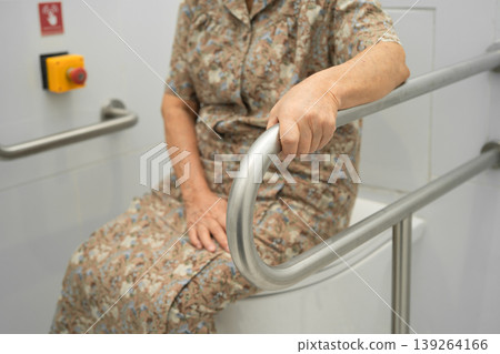 Asian elderly woman patient use toilet support rail in bathroom. Asian elderly woman patient use toilet support rail in bathroom. 139264166