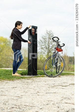 Female cyclist pumping up a wheel at a public repair point. Female cyclist pumping up a wheel at a public repair point. 139264370