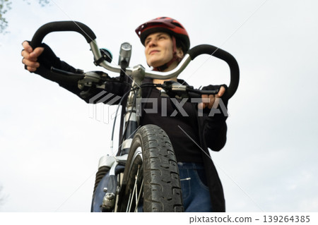 Confident young woman cyclist holding handlebars and looking into the distance Confident young woman cyclist holding handlebars and looking into the distance 139264385