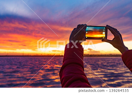 Hand photographing seascape at sunset with mobile phone 139264535