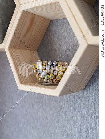 A young woman places a glass bowl filled with used batteries onto a wooden shelf for future disposal. This process demonstrates conscious household waste sorting and care for the environment. A young woman places a glass bowl filled with used batteries onto a wooden shelf for future disposal. This process demonstrates conscious household waste sorting and care for the environment. 139264732