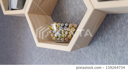 A young woman places a glass bowl filled with used batteries onto a wooden shelf for future disposal. This process demonstrates conscious household waste sorting and care for the environment. A young woman places a glass bowl filled with used batteries onto a wooden shelf for future disposal. This process demonstrates conscious household waste sorting and care for the environment. 139264734