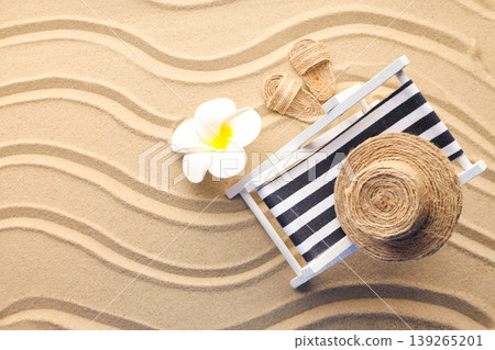 A lounge chair sits on the sand with a flower nearby A lounge chair sits on the sand with a flower nearby 139265201