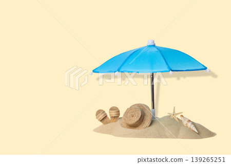 Blue umbrella stands over sand with seashells and summer items Blue umbrella stands over sand with seashells and summer items 139265251
