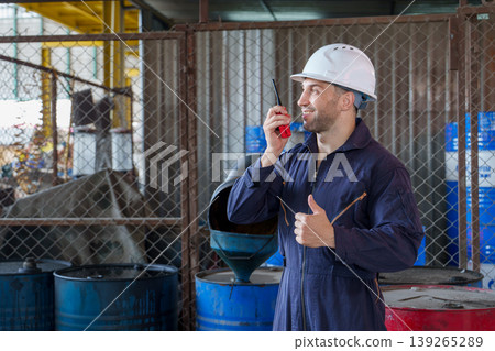 Mid-adult Caucasian male warehouse supervisor in navy coveralls giving a thumbs up and holding a radio transmitter in an Asian industrial facility. 139265289