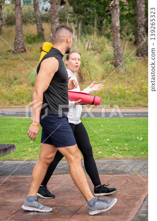 Active couple walking in park after workout carrying yoga mats Active couple walking in park after workout carrying yoga mats 139265323