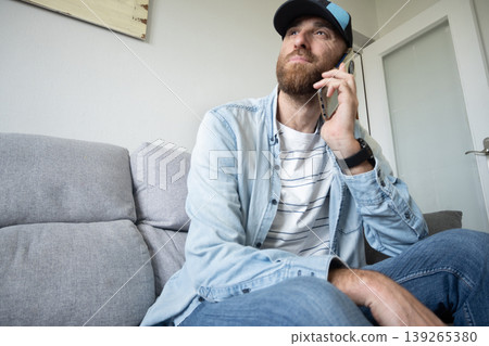 Man talking on smartphone sitting on sofa at home, casual lifestyle Man talking on smartphone sitting on sofa at home, casual lifestyle 139265380