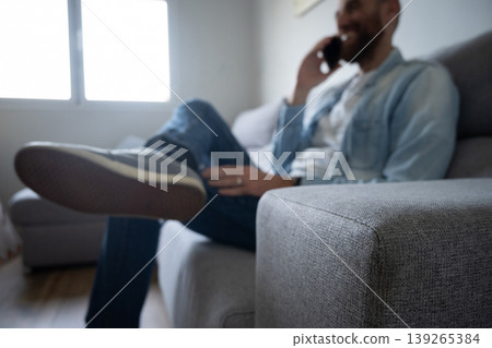 Man talking on smartphone sitting on sofa at home, relaxed lifestyle scene Man talking on smartphone sitting on sofa at home, relaxed lifestyle scene 139265384