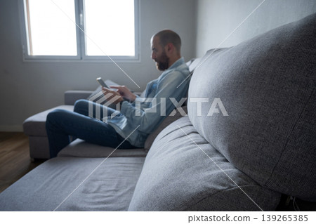 Man using smartphone sitting on sofa at home, relaxed lifestyle with copy space Man using smartphone sitting on sofa at home, relaxed lifestyle with copy space 139265385