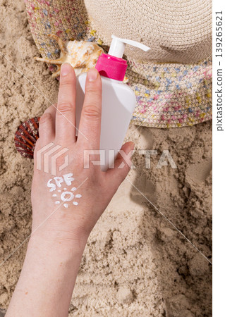 Woman applying sun cream with spf text on hand at beach. Skincare routine before sunbathing during summer holiday. Protection against ultraviolet radiation and sunlight. Concept of healthy skin care. Woman applying sun cream with spf text on hand at beach. Skincare routine before sunbathing during summer holiday. Protection against ultraviolet radiation and sunlight. Concept of healthy skin care. 139265621