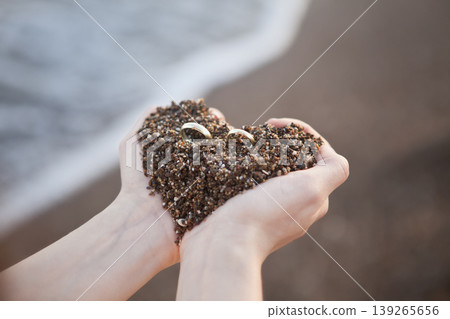 Romantic Wedding Rings on Sand Heart Concept. Marriage Symbol Rings on Heart Shaped Sand Close Up. Romantic Wedding Rings on Sand Heart Concept. Marriage Symbol Rings on Heart Shaped Sand Close Up. 139265656