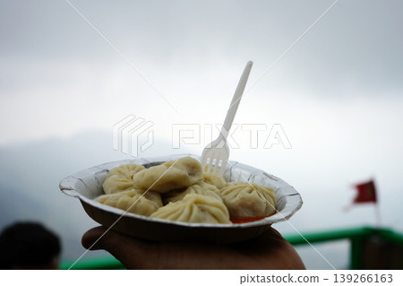 Hand holding a plate of fresh steamed momos with a mountain view backdrop Hand holding a plate of fresh steamed momos with a mountain view backdrop 139266163