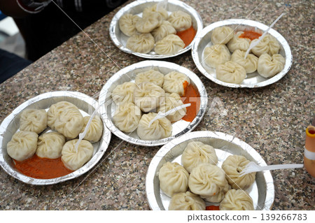 Multiple plates of delicious steamed momos with spicy red chutney served for a group 139266783