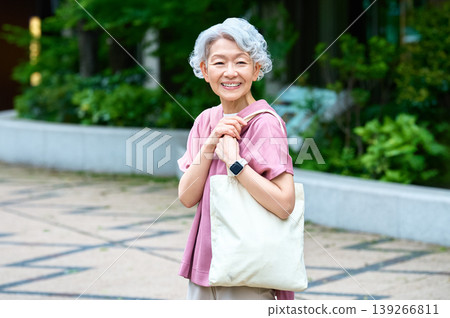 A senior woman smiling, carrying a white tote bag. A senior woman smiling, carrying a white tote bag. 139266811