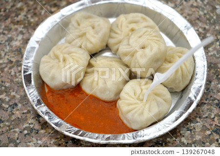 Freshly steamed traditional momos served with spicy red chutney on a disposable foil plate 139267048