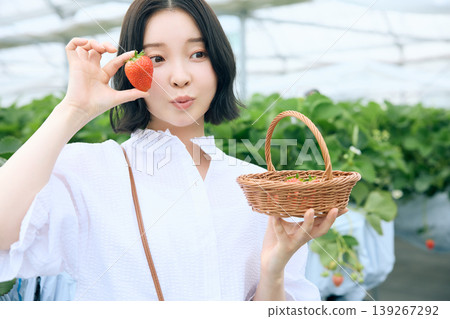 年輕女子享受採摘草莓的樂趣；日本女子在溫室裡手持新鮮採摘的草莓，笑容燦爛。 139267292