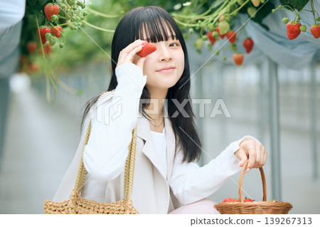 年輕女子享受採摘草莓的樂趣；日本女子在溫室裡，手持新鮮採摘的草莓，笑容燦爛。 139267313
