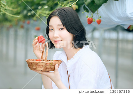 年輕女子享受採摘草莓的樂趣；一位日本女子在溫室裡微笑，手裡拿著新鮮採摘的草莓。 139267316