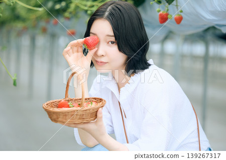 A young woman with a smile holding freshly picked strawberries at a strawberry picking farm; a Japanese woman with short hair enjoying spring leisure activities. A young woman with a smile holding freshly picked strawberries at a strawberry picking farm; a Japanese woman with short hair enjoying spring leisure activities. 139267317