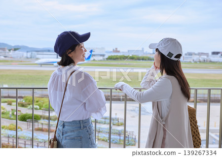 兩名年輕女子在機場觀景台上一邊觀看飛機一邊愉快地交談——旅行/郊遊圖片 139267334