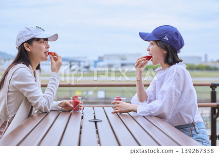 Two young women eating strawberries on an outdoor terrace. 139267338