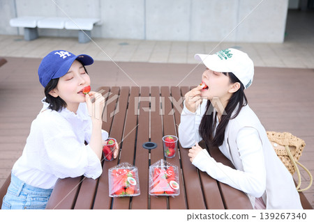 Two women eating fresh strawberries at an outdoor table. 139267340