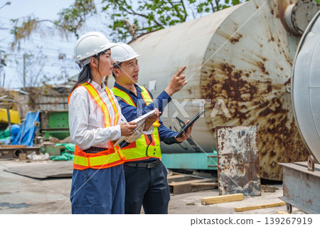 Asian male and female engineers inspecting an industrial site with large storage tanks. 139267919