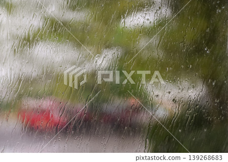 Raindrops and water streams on window glass with blurred colorful background Raindrops and water streams on window glass with blurred colorful background 139268683
