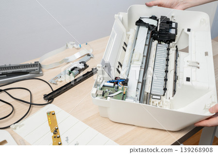 A technician services a disassembled office printer, exposing rollers, circuit boards and cables during maintenance and troubleshooting to repair paper feed and electronic components. 139268908