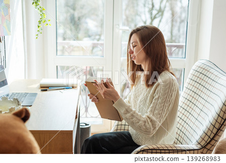 Woman unboxing delivered package on desk at home Woman unboxing delivered package on desk at home 139268983