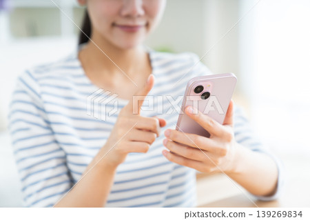 A young woman's hands as she uses her smartphone in the living room A young woman's hands as she uses her smartphone in the living room 139269834