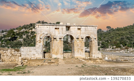 The Roman Arch of Modestus rising over excavated ruins at ancient Patara archaeological site, Lycia, Turkey. A well-preserved triumphal gate under dramatic sunset sky 139270833