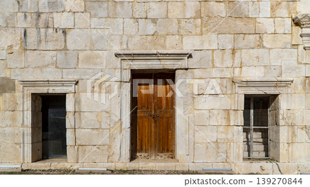 Ancient limestone facade with a locked wooden double door and framed window niches at the Patara archaeological site, Antalya, Turkey Ancient limestone facade with a locked wooden double door and framed window niches at the Patara archaeological site, Antalya, Turkey 139270844