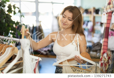Young woman chooses dresses and tops in store Young woman chooses dresses and tops in store 139271743
