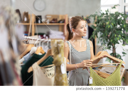 Young woman chooses a set of clothes for the summer. Visitor to the boutique examines new summer collection of clothes Young woman chooses a set of clothes for the summer. Visitor to the boutique examines new summer collection of clothes 139271778