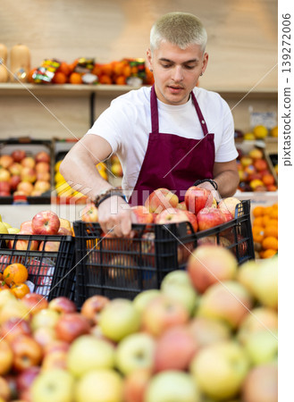 Young guy seller puts apples in vegetable shop Young guy seller puts apples in vegetable shop 139272006