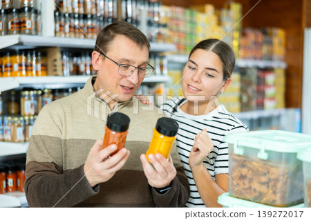 Man and girl are discussing choice of spices between two options while standing in supermarket Man and girl are discussing choice of spices between two options while standing in supermarket 139272017