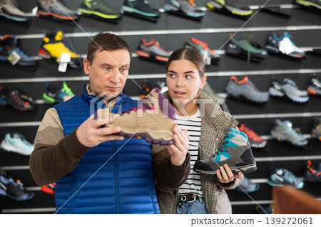 Man and young girl chooses winter sport shoes together for an hiking trip in sports store Man and young girl chooses winter sport shoes together for an hiking trip in sports store 139272061