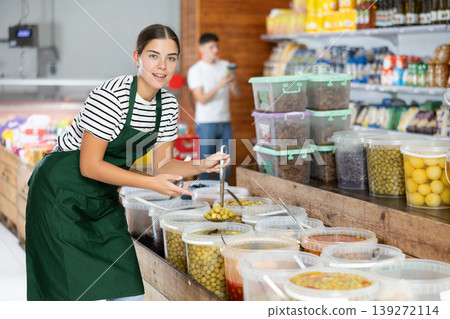 Young girl in supermarket, scooping marinated olives from bucket with ladle Young girl in supermarket, scooping marinated olives from bucket with ladle 139272114