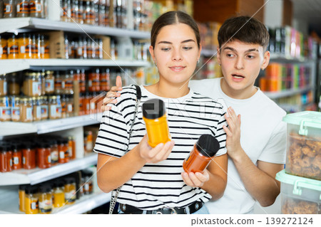 Cheerful young couple choosing spices in glass jars in supermarket Cheerful young couple choosing spices in glass jars in supermarket 139272124